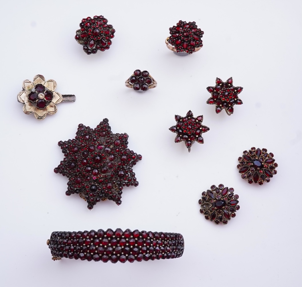 A suite of garnet and paste jewellery, comprising: a brooch, 5cm diameter; a bangle, inner circumference 16cm; two rings, sizes I and M; a pair of earrings, and a single earring, each set with rose-cut garnets; and a pai
